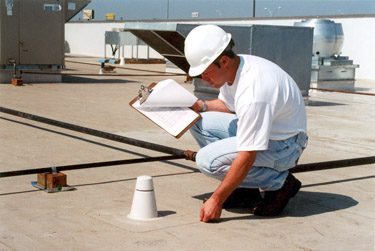 A man in white shirt and hard hat writing on paper.